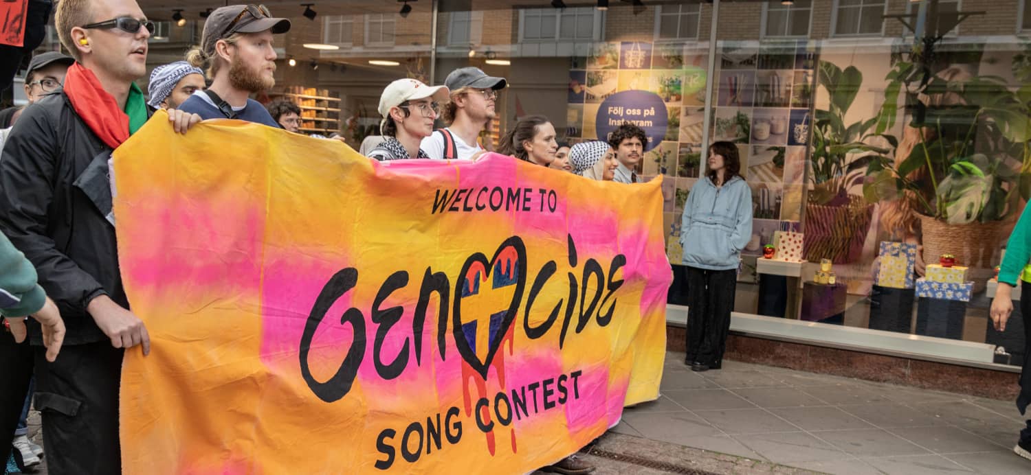Manifestantes pro-palestinos sostienen una pancarta naranja y rosa con el mensaje "Welcome to Genocide Song Contest" frente a la Malmö Arena.