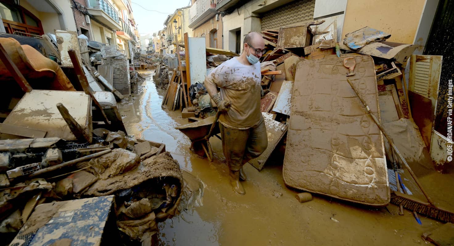 Un hombre con mascarilla arrastra una carretilla entre el barro y los escombros en una calle de Paiporta