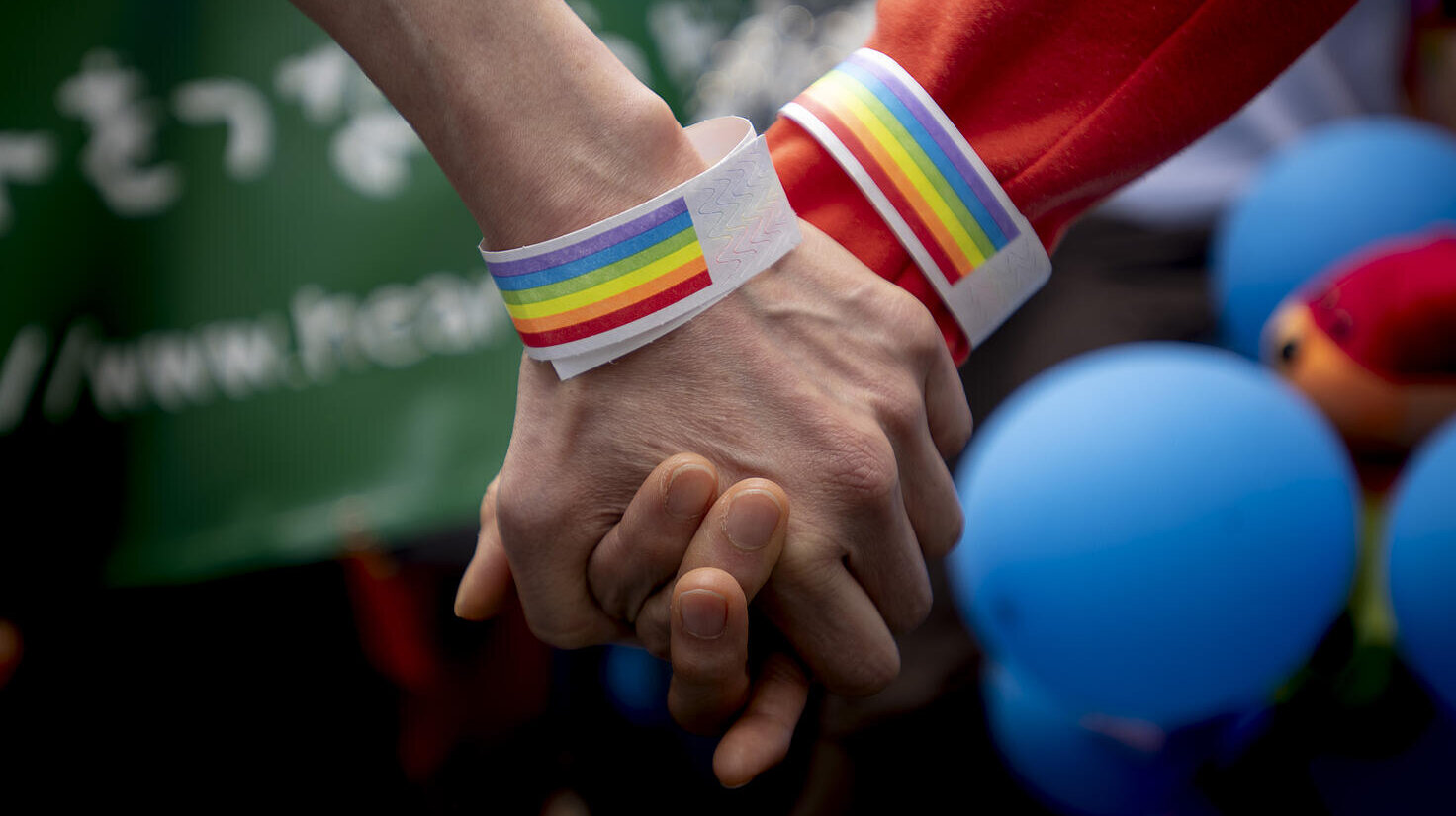 Dos manos enlazadas, con brazaletes con bandera gay en manifestación en Tokio