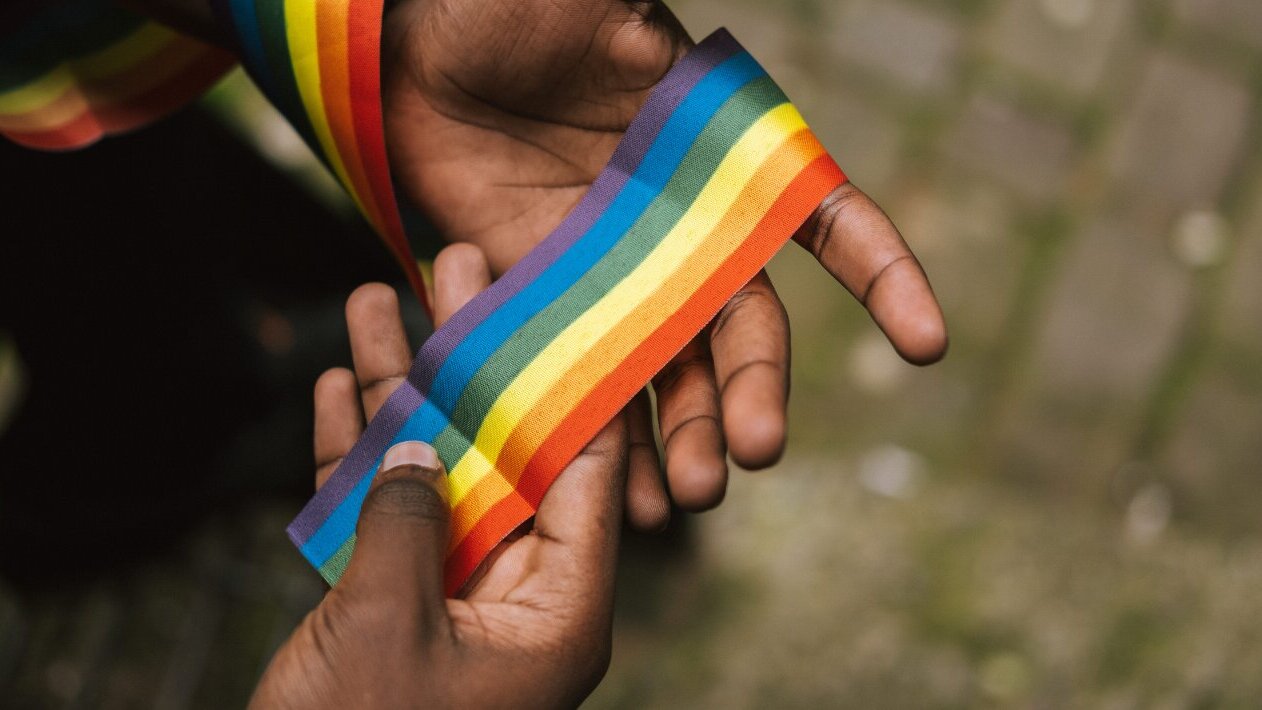 Una mano sostiene un lazo con los colores del arcoiris