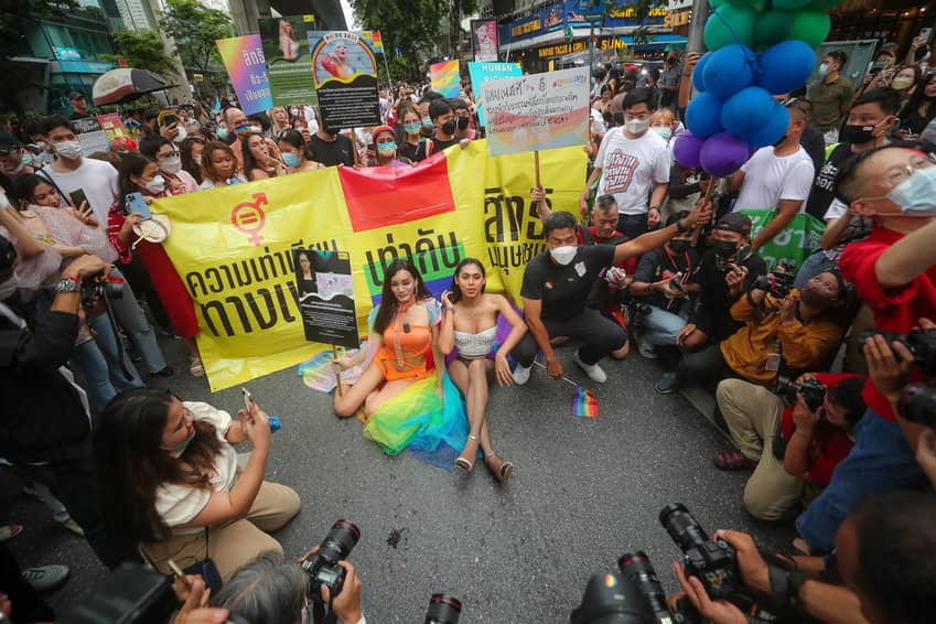 Varias personas se sientan en la calle, exhibiendo con orgullo una bandera arco iris.