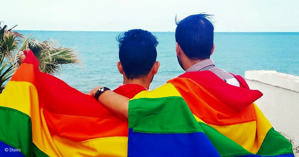 Dos hombres portando la bandera arcoiris abrazados