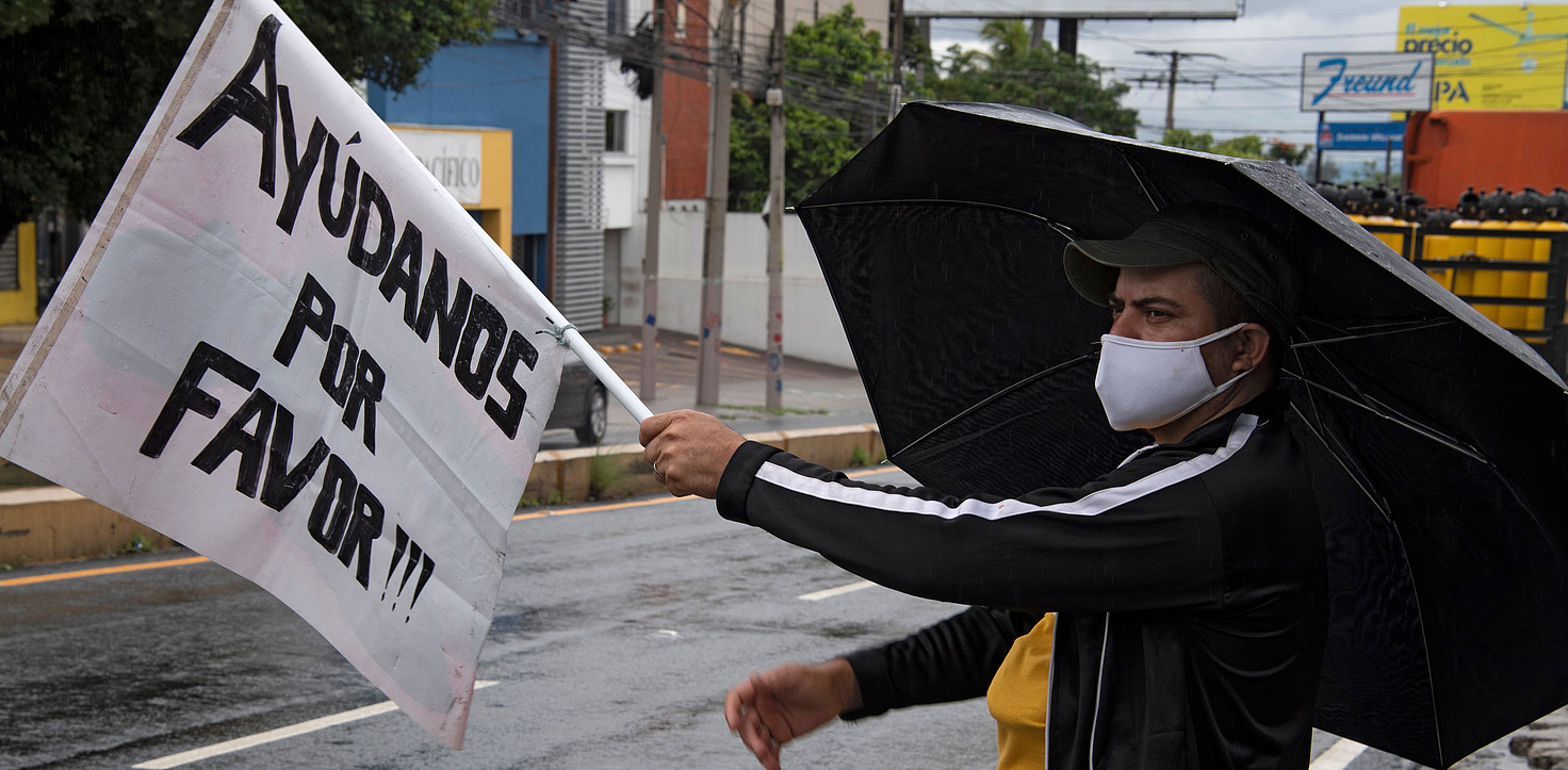 Un hombre ondea una bandera blanca que dice "Ayúdenos por favor" en una carretera en San Salvador el 05 de junio de 2020.