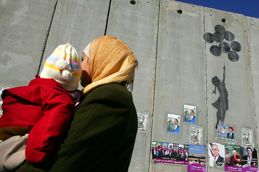 Una mujer palestina camina frente a un grafiti de Banksy