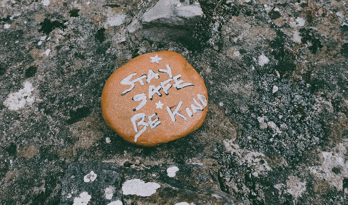Un piedra tiene escrito el texto "Be safe, be kind" (estate a salvo, sé amable)