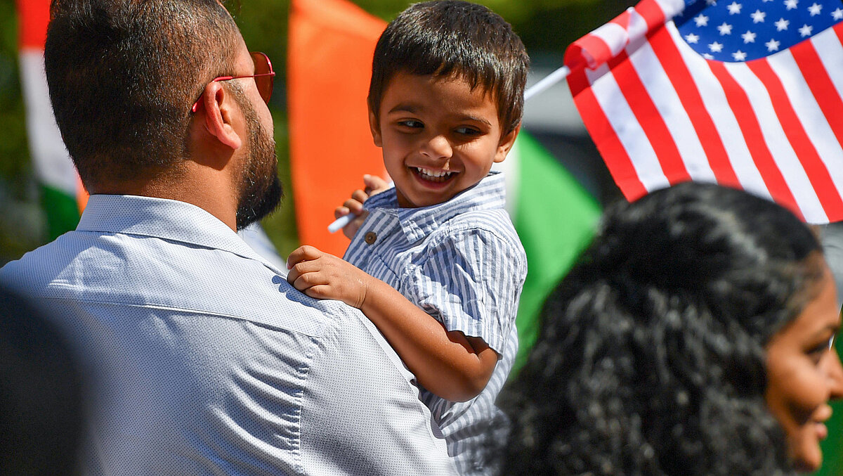 Un niño pequeño en brazos de su padre lleva una bandera estadounidense en la mano