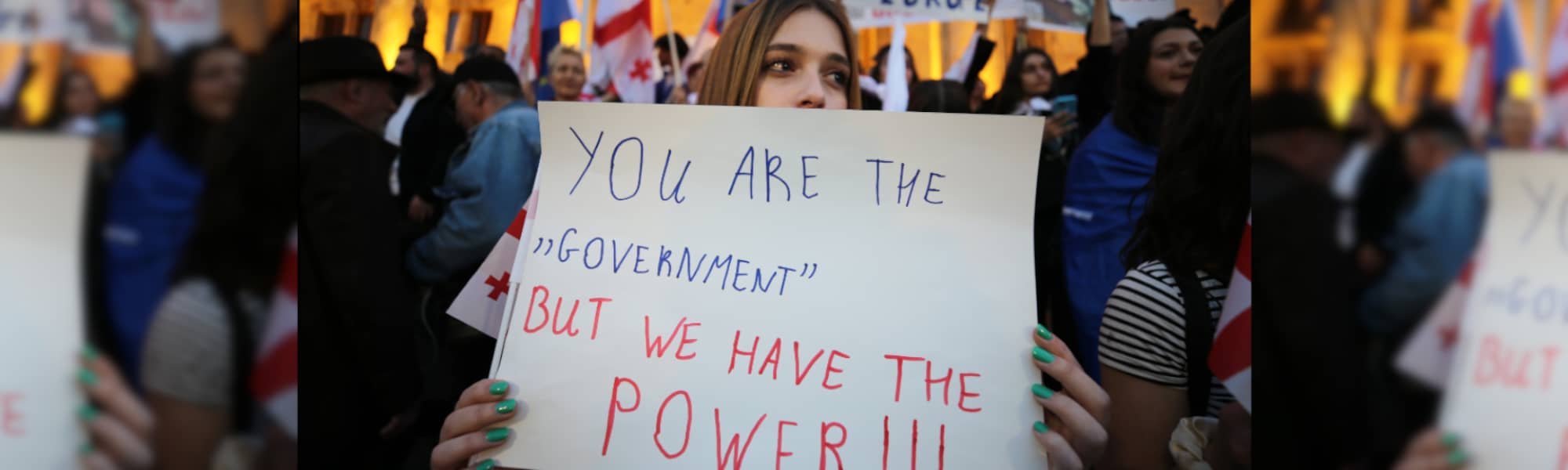 Una chica joven sostiene un cartel que pone "Vosotros sois el gobierno, pero nosotros tenemos el poder"