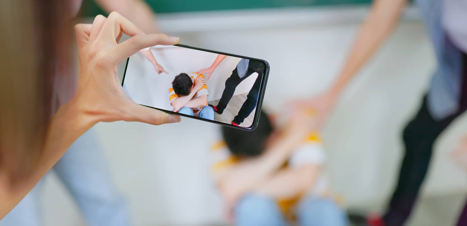 Una persona joven graba con su móvil una escena de acoso escolar