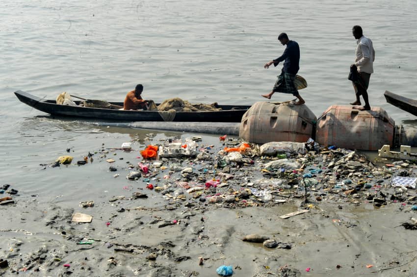 Pescadores en una embarcación rodeados de residuos plásticos y contaminación en el río Karnaphuli, Bangladés.