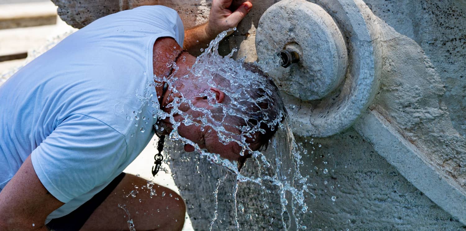 Hombre se moja la cara en una fuente pública para aliviarse de las altas temperaturas