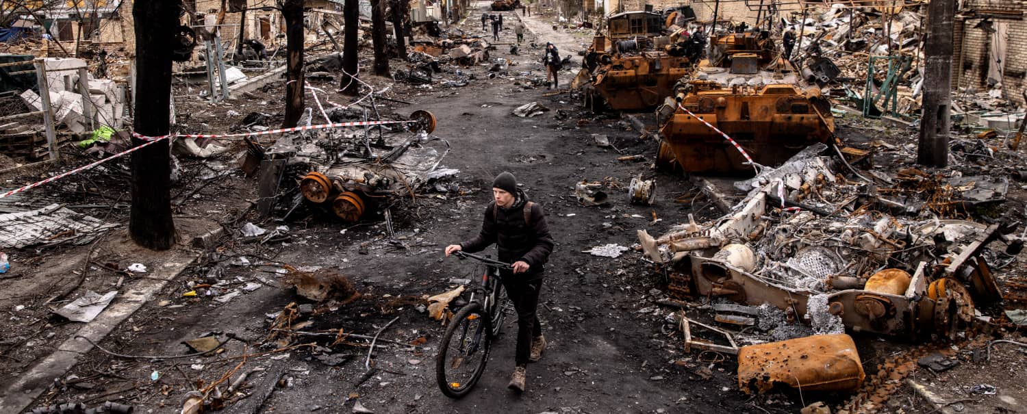 Un hombre empuja su bicicleta entre escombros y vehículos militares rusos destruidos