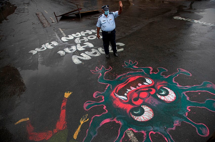 Un policía indio se encuentra junto a un grafiti pintado para crear conciencia sobre el coronavirus en Gauhati, India