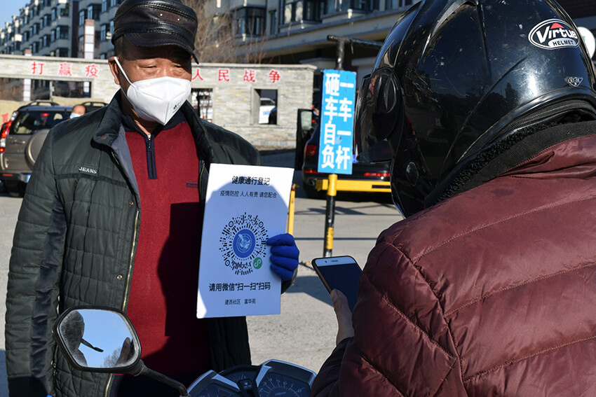 Un voluntario sostiene un cartel con un código QR para indicar el estado de salud en una entrada a un complejo residencial en Suifenhe