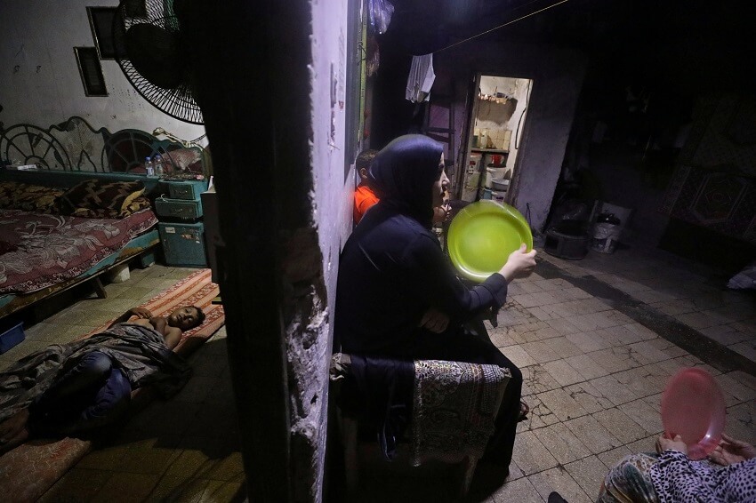 Una mujer palestina usa una bandeja de plástico para refrescarse en un día caluroso durante un corte de energía mientras un niño duerme dentro de su casa que está iluminada por luces que funcionan con baterías después de que la única planta de energía de Gaza cerró en medio de la tensión con Israel, en el campo de refugiados de Jabalia , en el norte de la Franja de Gaza el 23 de agosto de 2020. 