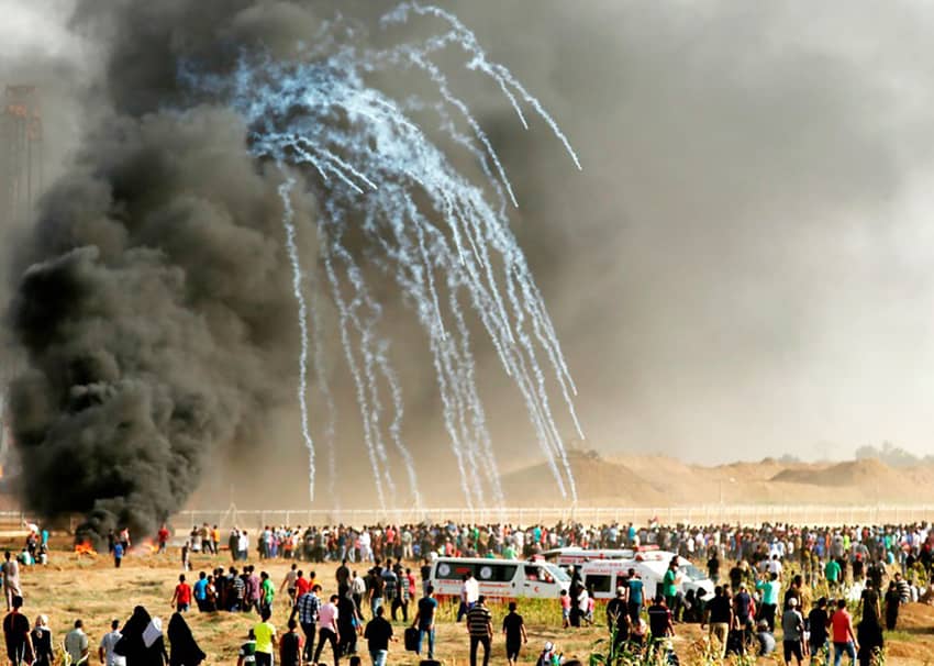 Manifestantes palestinos corren para ponerse a cubierto de los botes de gas lacrimógeno lanzados por Israel