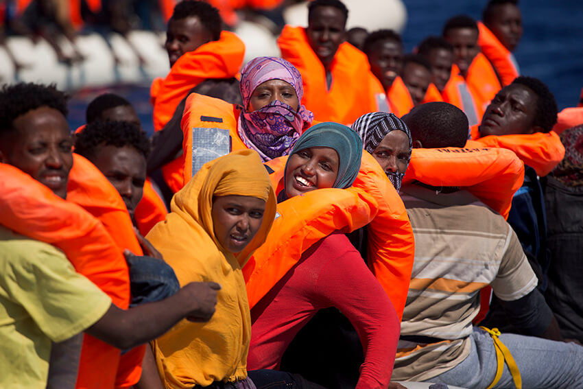 Varias mujeres migrantes sonríen a bordo de un bote mientras navegan en el mar Mediterráneo hacia las costas italianas