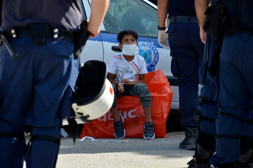 un niño mira a los policías mientras espera para entrar en un autobús desde el campo de refugiados de Kara Tepe hacia el puerto de Mitilene, en la isla nororiental de Lesbos, Grecia.