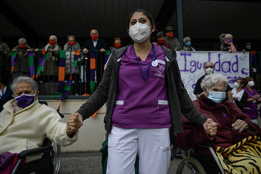 Una trabajadora sanitaria de una residencia de ancianos da la mano a dos personas mayores. 