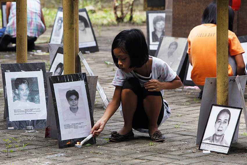 Una niña enciende una vela cerca de una serie de fotos de personas desaparecidas en un santuario conmemorativo levantado por la organización no gubernamental Familias de Víctimas de Desapariciones Involuntarias (FIND), en Manila. 