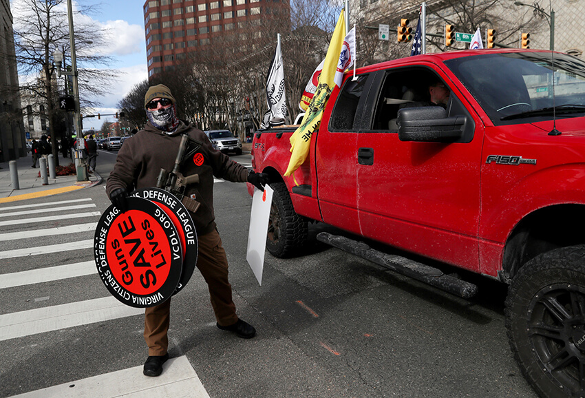 Un hombre sostiene carteles que dicen "Las armas salvan vidas" mientras una caravana de automóviles pasa en apoyo de la segunda enmienda cerca del Capitolio del estado de Virginia el Día del Lobby, un día tradicionalmente reservado para que el público ejerza presión sobre los legisladores, el 18 de enero de 2021.