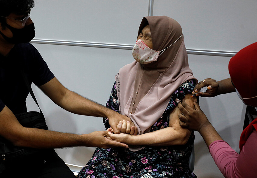 Mirza Amir, de 38 años, coge la mano de su madre Saleha Bt Mohamed, de 76 años, mientras se vacuna contra la COVID-19 en Singapur, el 8 de marzo de 2021.