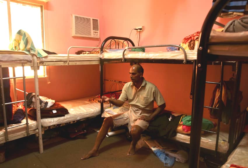 Trabajador migrante sentado en una de las camas de la habitación que comparte con otros siete trabajadores indios en Doha (Qatar)