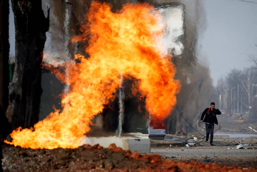 Un hombre pasa junto a una tubería de gas en llamas que fue alcanzada durante un bombardeo.