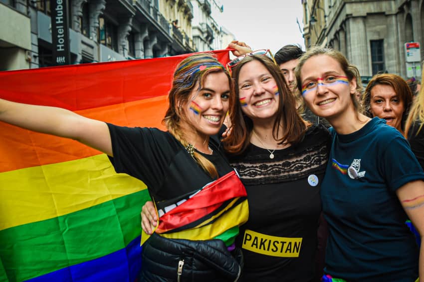  Tres mujeres felices junto a una bandera arco iris posan para una foto