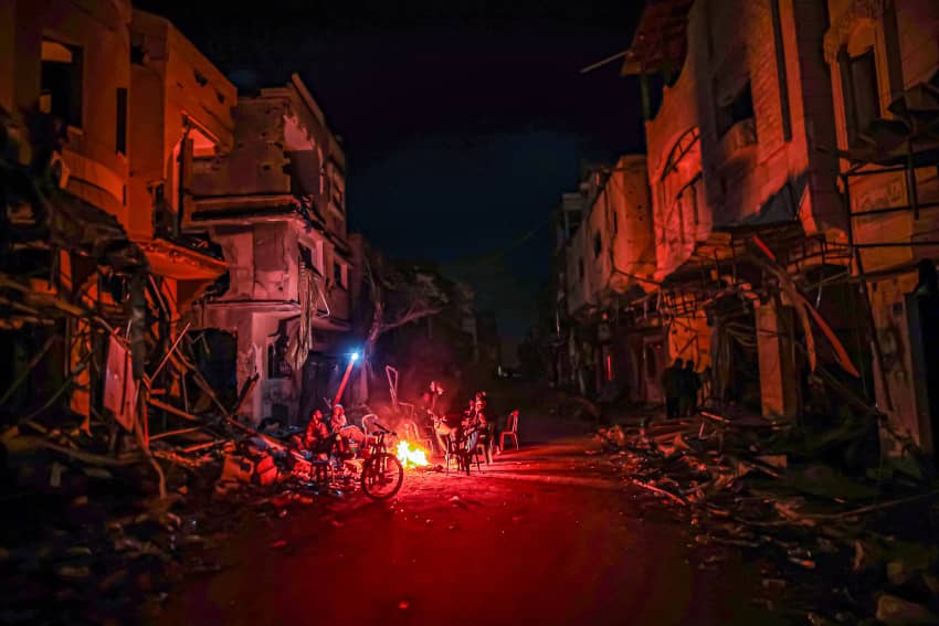Ante los apagones de luz, una familia se calienta con un fuego en la calle en Gaza