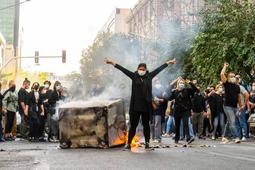 Una mujer con los brazos extendidos reclama atención frente a un cubo de basura en llamas durante una manifestación en Teherán