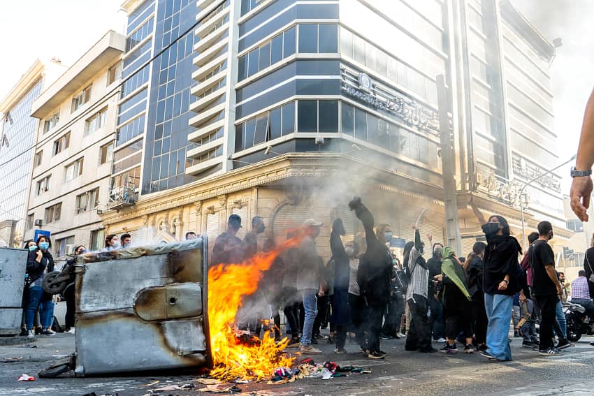 Varios manifestantes con el brazo el alto caminan junto a un cubo de basura en llamas en Teherán, Irán.