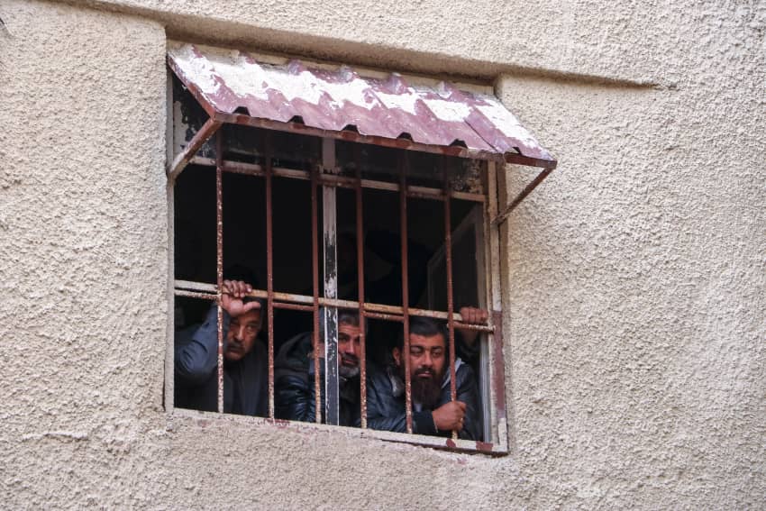 Varios prisioneros miran a través de una vertana con barrotes desde la cárcel de Saydnaya