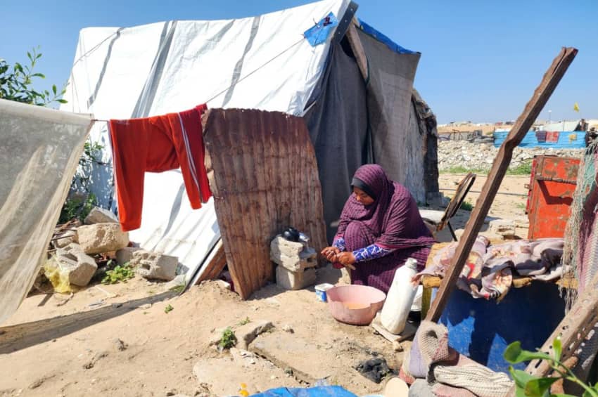 Mujer en un campamento improvisado en Khan Yunis, Gaza, usando una pequeña cantidad de agua para tareas básicas.