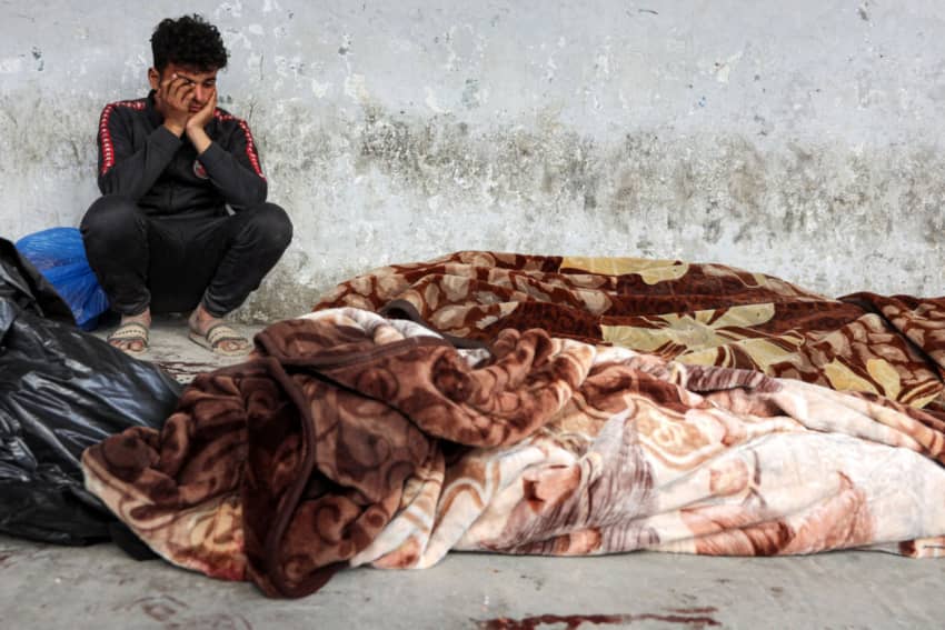 Niño llorando junto a cuerpos cubiertos con mantas en el hospital Al-Ahli de Ciudad de Gaza, tras un bombardeo israelí el 18 de marzo de 2025. Más de 220 personas murieron en el ataque, según equipos de rescate.