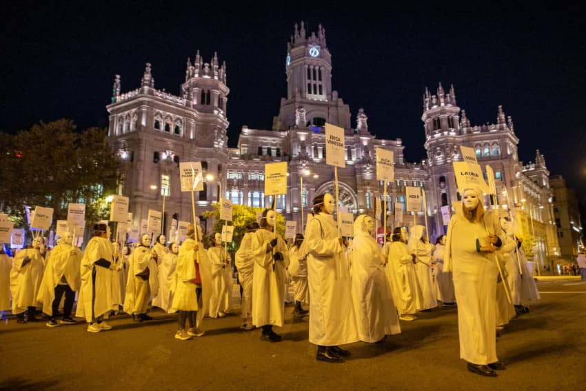Un grupo de mujeres con máscaras blancas y pancartas marchan durante una manifestación feminista