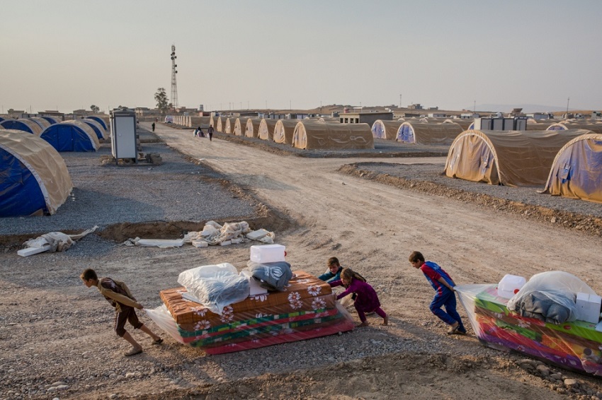 Niños iraquíes desplazados transportan colchones y otros útiles en el campamento de Hasansham