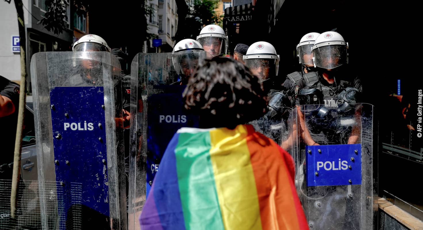 Un manifestante que porta una bandera arcoíris frente a policías antidisturbios