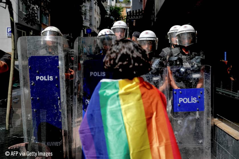 Un manifestante que porta una bandera arcoíris frente a policías antidisturbios